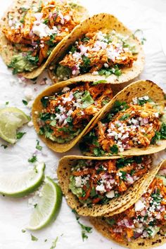 four fish tacos with cilantro, limes and shredded cheese on top