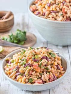 two bowls filled with macaroni salad on top of a white wooden table next to other dishes