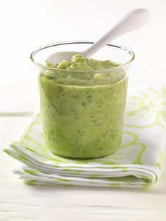 a small glass bowl filled with green sauce on top of a napkin next to a spoon