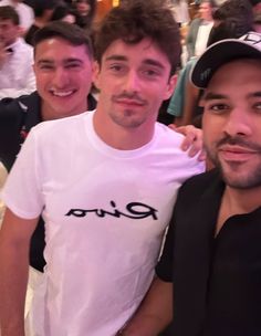 three men are posing for the camera in front of a crowd at an event, one is wearing a riva t - shirt and the other has his arm around his neck