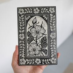 a hand holding up a black and white card with floral designs on the front cover