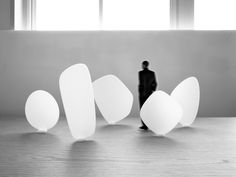 a black and white photo of a person standing in front of three large, oval shaped objects