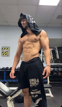 a shirtless man with no shirt standing in the gym wearing shorts and a hoodie