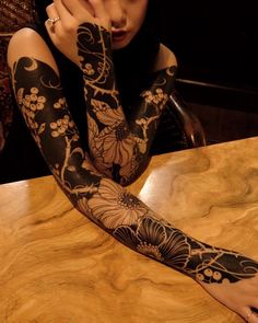 a woman sitting at a table with her arm covered in black and white tattoo designs