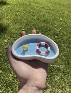 a hand is holding a small bowl with a rubber duck in it and a life preserver