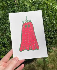 a hand holding up a card with a strawberry on it in front of some bushes