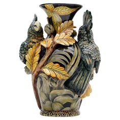 a vase with two birds sitting on it's side and leaves around the base