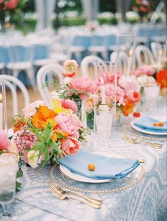 the table is set with blue linens and gold place settings, pink and orange flowers