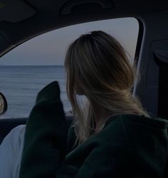 a woman sitting in the passenger seat of a car looking out at the ocean from inside