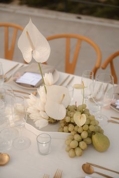 the table is set with white flowers, grapes and silverware