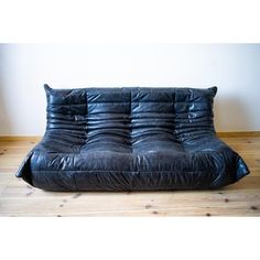 a black leather futon couch sitting on top of a hard wood floor next to a white wall