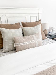 a white bed topped with lots of pillows next to a night stand and nightstands