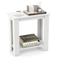 a small white table with books and a cup on the top, next to a stack of books