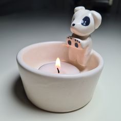 a small teddy bear sitting in a white bowl with a lit candle on the side