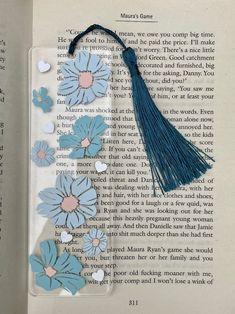 an open book with a tassel and blue flowers on the pages, next to a pair of scissors