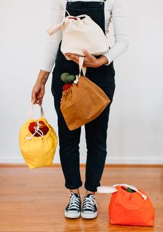 a woman is holding two bags in one hand and an orange bag in the other