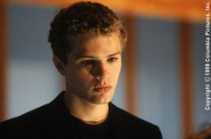 a young man with curly hair looking at the camera while wearing a black t - shirt