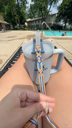 someone is tying a colorful tie around a coffee cup on the edge of a swimming pool