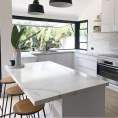 a kitchen with white counter tops and black pendant lights over the stove top, along with three stools