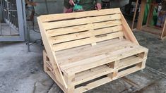 a wooden bench made out of pallets sitting on top of cement floor next to a building