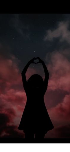 the silhouette of a woman holding her hands up in the shape of a heart against a night sky