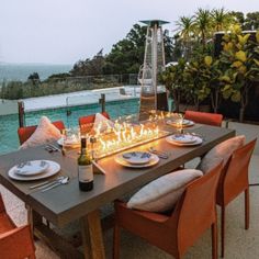 an outdoor dining table set with plates and wine glasses on it next to a swimming pool