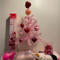 a pink christmas tree with hearts on it and other decorations in front of a white wall