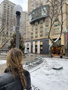 a woman is sitting on a bench in the middle of a snowy city park area