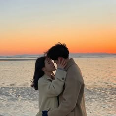 a man and woman are kissing on the beach at sunset, with water in the background