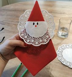 a person holding up a paper santa clause on top of a wooden table with plates and glasses