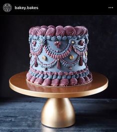 a blue and pink cake sitting on top of a wooden table next to a gold plate