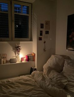 an unmade bed with white sheets and pillows in front of a window at night