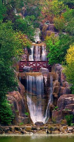 a waterfall with a bridge over it surrounded by trees