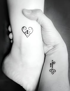 two people holding hands with tattoos on their arms and one has a key to the heart