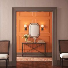 an orange room with two chairs and a table in front of the mirror on the wall