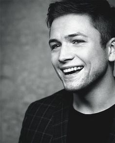 a black and white photo of a young man smiling at the camera with his head tilted to the side