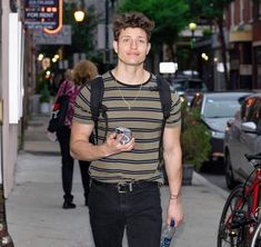 a young man is walking down the street holding a drink and looking at the camera