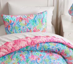 the comforter and pillows are all colorfully decorated with pink, blue, and green leaves