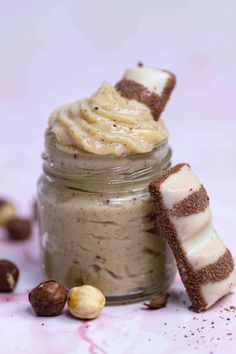 a jar filled with some kind of dessert on top of a white table next to nuts