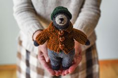 a person holding a small stuffed animal wearing a sweater and hat with buttons on it