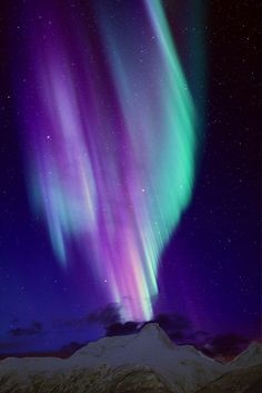 an aurora bore is seen in the night sky above snow covered mountains and clouds, with bright