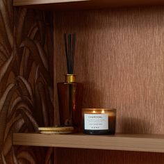 a candle sits on a shelf next to a vase with a reed diffuse in it