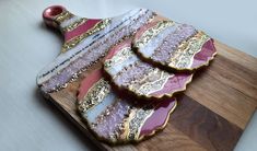 three pieces of pink and gold decorated cookies on a wooden cutting board