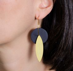 a woman wearing black and yellow earrings with two leaves hanging from it's sides