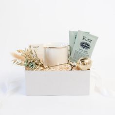 a white box filled with various items on top of a white table next to a cup and saucer