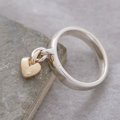 Add charm to your jewellery collection with our exquisite and unique solid silver ring, adorned with a delicate sweetheart recycled gold heart charm that gracefully sways with your every move. This everyday yet extraordinary ring is destined to spark conversations and become a cherished part of your personal style. Craftsmanship: Meticulously crafted using traditional lost wax casting techniques, our solid sterling silver rings are designed for both aesthetics and comfort. The ring features a robust and enduring loop on the front, while its generous band shape prioritizes comfort, durability, and contemporary elegance. The dangling heart charm is crafted from your choice of either recycled solid rose gold, or recycled solid yellow gold, with a beautifully rounded, organic shape. Quality As Charm Rings Dangle, Chunky Silver Rings, Gold Heart Ring, Charm Ring, Unusual Rings, Silver Signet Ring, Rose Gold Heart, Designer Fashion Jewelry, Charm Rings