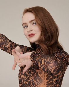 a woman with red hair and blue eyes pointing to the side while wearing a leopard print top