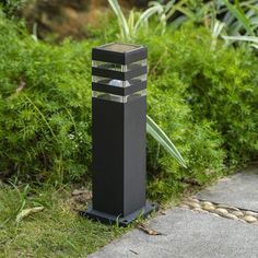 a black sculpture sitting on top of a sidewalk next to green grass and bushes in the background