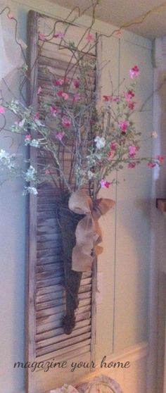 a vase filled with pink flowers sitting on top of a wooden shelf next to a window