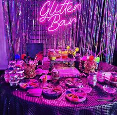 a table topped with lots of food under a neon lit sign that reads glitter bar